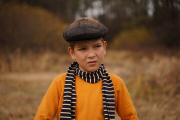 Portrait of a cute teenager in a retro cap and a striped scarf against the backdrop of an autumn forest.