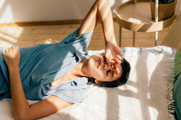 A woman lies relaxed on a bed in the light of summer sunbeams.