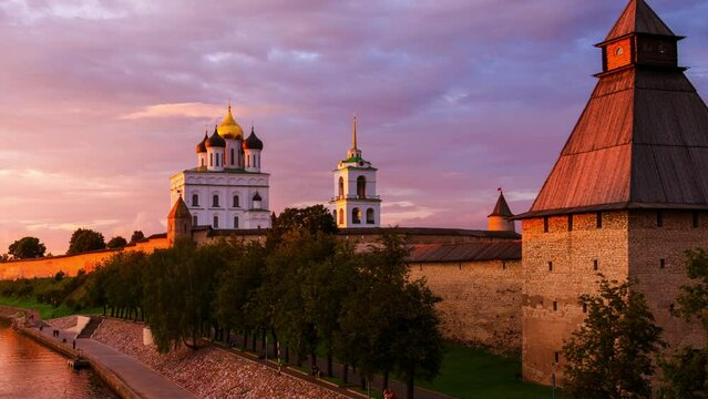 Pskov, Russia. Illuminated Pskov Kremlin at sunset. Popular landmark in Russia. Time-lapse of a colorful sky over a river and promenade area. Zoom in