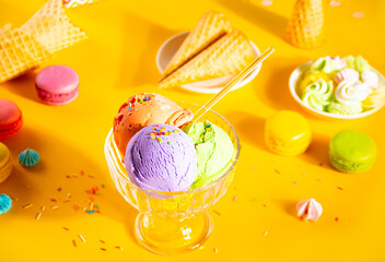 Various colorful ice cream scoops or balls sundae dish with waffle cones, macaroons on yellow background