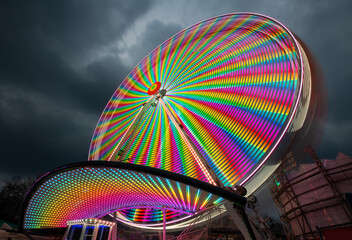 Ferris wheel on a german funfair “Kirmes“ or „Jahrmarkt“ at night with many colorful lights. Long time exposure that effects multi color light traces and abstract paintings at evening twilight.