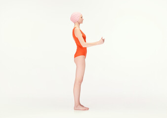 Young girl in red swimsuit and swimming cap standing with hands holding together isolated over white background. Side view. Concept of retro style, sport, fashion, youth, vintage. Copy space for ad