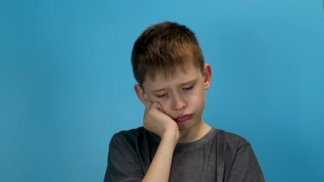 portrait of a tired caucasian boy 8-9 years old, bored against a blue background. Exhausted european schoolboy with a sad expression. The concept of fatigue and exhaustion