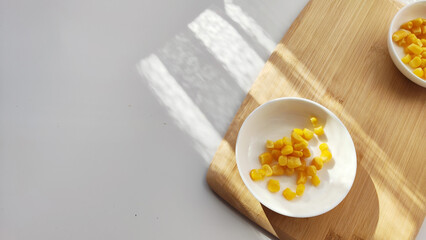 Lot of pieces of canned yellow corn on plate which is on wooden bamboo cutting board on white background. The concept of cooking and delicious healthy food