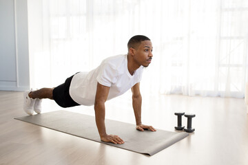 Motivated african man exercising at home, planking