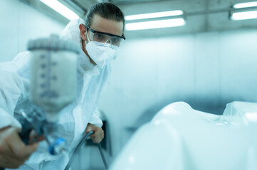 Auto mechanic in car spray room giving the spray nozzle injected into the car front bumper of the...