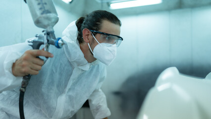 Auto mechanic in car spray room Inspecting the paint sprayed into the front bumper of the car that...