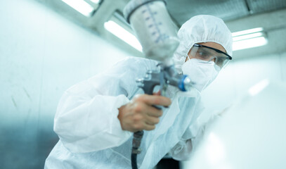 Auto mechanic in car spray room giving the spray nozzle injected into the car front bumper of the...