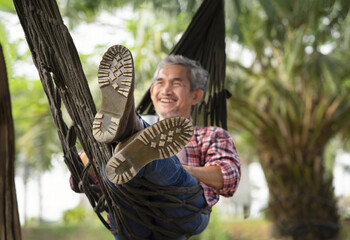 mature man legs in boots laying on rope hammock, happy senior male relaxing at resort garden on summertime