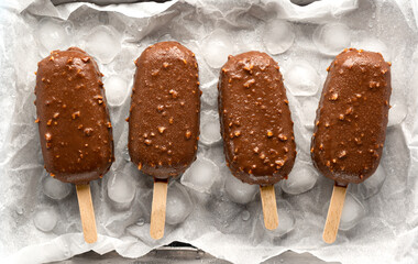 Popsicle ice cream in chocolate glaze with nuts, with ice and drops of water on the background. Close-up summer dessert eskimo, top view.