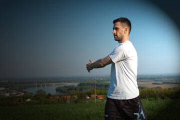 Fototapeta premium a young guy in a white shirt is stretching, behind him is a beautiful landscape, training in nature, a healthy lifestyle 