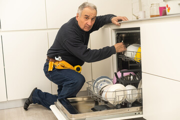 Male Technician Sitting Near Dishwasher In Kitchen