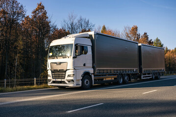 Truck is driving through the forest in autumn. Car transport . Truck with semi-trailer in gray color.