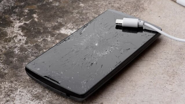 Crushed broken cell phone with charging cable on the concrete surface of the house