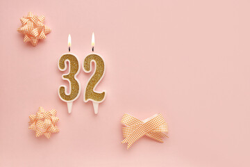 Fototapeta na wymiar Number 32 on a pastel pink background with festive decorations. Happy birthday candles. The concept of celebrating a birthday, anniversary, important date, holiday. Copy space. banner