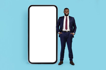 Online Offer. Smiling Black Businessman Posing Near Big Blank Smartphone