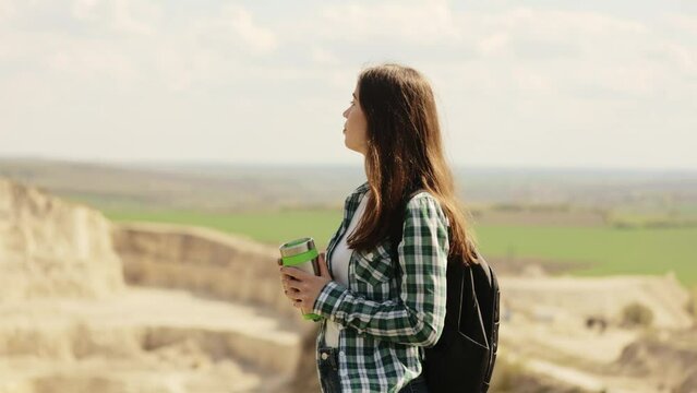 Young attractive woman hiker, backpacker hiker drinking hot tea or coffee and resting on top of mountain rock. Care for health, authenticity, a sense of balance and peace.