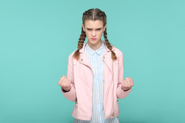 Portrait of angry aggressive attractive teenager girl with braids wearing pink jacket standing with...