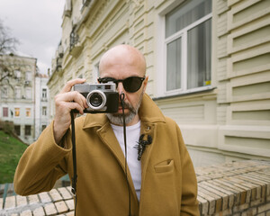 Handsome beard photographer makes pictures on film retro camera in the Kyiv city, Ukraine.