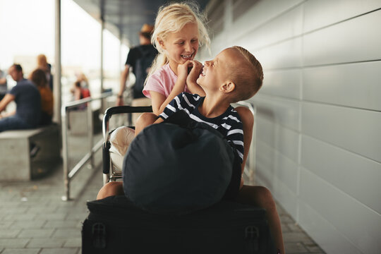 Laughing little brother and sister sitting on a luggage cart