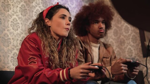 Diverse couple in retro clothes playing videogame using joysticks