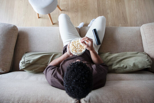 Unrecognizable man eating popcorn and watching TV on sofa