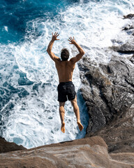 Man cliff jumping off Spitting Cave on Oahu, Hawaii. High quality photo
