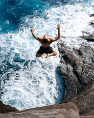 Man cliff jumping off Spitting Cave on Oahu, Hawaii. High quality photo
