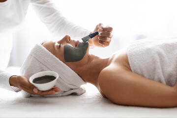 Side view of spa therapist applying clay mask on woman face
