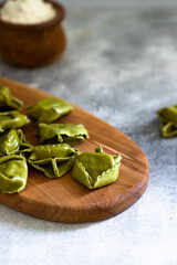 Homemade Italian tortellini with ricotta and spinach served on a wooden cutting board. A dish of classic Italian cuisine. Tortelloni di ricotta e spinaci. Close-up, selective focus