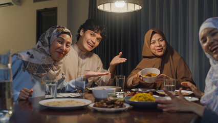 Happy Asian muslim family celebrate long distance with cousin looking at camera video call online Ramadan dinner together at home. Two generation celebration of Eid al-Fitr togetherness at home.