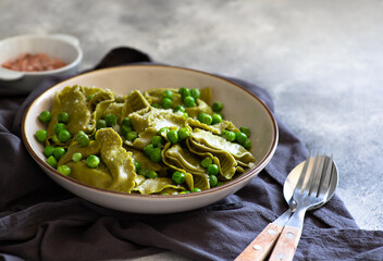 Homemade Italian tortellini with ricotta and spinach served with green pea sauce. A dish of classic Italian cuisine. Tortelloni di ricotta e spinaci. Close-up, selective focus