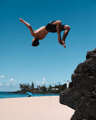 Man cliff diving and flipping at Waimea Bay on Oahu, Hawaii in the summer.