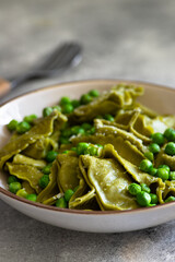 Homemade Italian tortellini with ricotta and spinach served with green pea sauce. A dish of classic Italian cuisine. Tortelloni di ricotta e spinaci. Close-up, selective focus