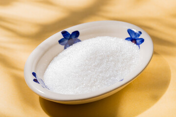plate with heap of white sugar on the yellow background, top view