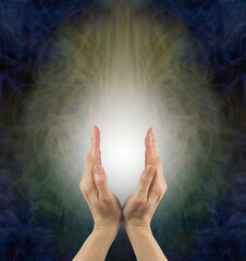 Shamanic female healer sending healing vibes - mature woman's hands with white light between against an ethereal energy field background with copy space
