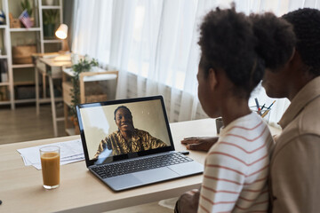 Naklejka na ściany i meble Military mom having video call with her family, they sitting at table in front of laptop and talking to her