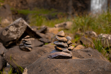 Pilha de pedras em uma cachoeira com rochas atrás em tons de marrom e água caindo em um lago