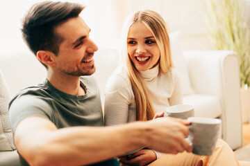 Beautiful young happy couple enjoying coffee at home on sofa