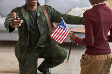 Close-up of little girl with american flag meeting her military dad at home, he coming back from...