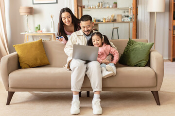 Asian Family Shopping Online Using Laptop And Credit Card Indoors