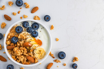 Bowl of oat granola with yogurt, banana, blueberries, chia seeds and nuts on white background for...