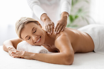 Fototapeta na wymiar Beautiful middle aged woman receiving relaxing shoulder massage in spa salon