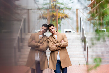 Portrait of stylish handsome young man with coat standing outdoors and leaning on wall.