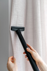 Woman hands with vacuum cleaner wash curtains in living room