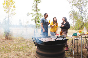 Lively Latin American Trio Enjoying a Barbecue Picnic with Beer and Good Company in the Countryside