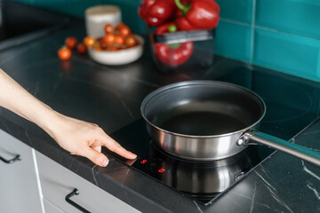 woman prepare dinner on electrical hob at modern kitchen, closeup