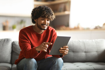 Handsome young indian guy using digital tablet at home