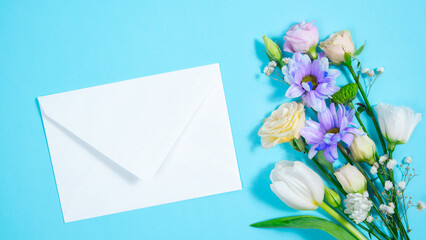 Natural flowers appear on blue background and form bouquet. White envelope appears next to it.