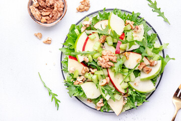 Waldorf salad with red and green apple, green celery, lettuce, arugula and walnuts on plate, white table background, top view